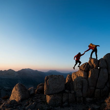 Two climbers helping one another climb up rocks 